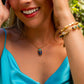 Woman wearing a blue top and gold necklace with a blue pendant, outdoors.