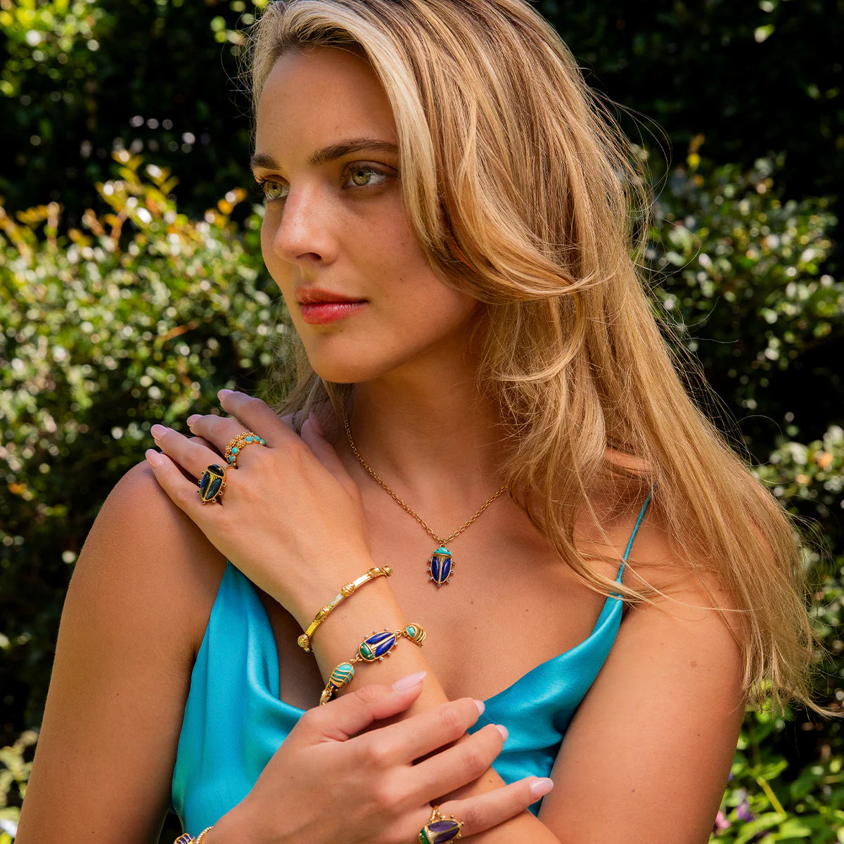 Woman wearing colorful jewelry outdoors with greenery in the background