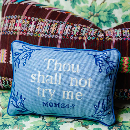 A blue needlepoint pillow with the text 'Thou shall not try me' and the Bible verse 'MOM 24:7' embroidered on it, placed on a patterned surface.