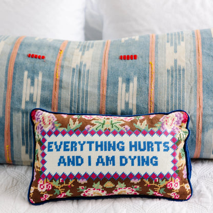 Decorative pillow with embroidered text 'Everything hurts and I am dying' on a patterned background.