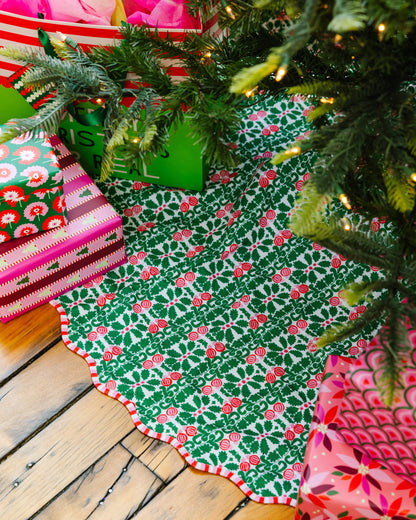 Green and red patterned Christmas tree skirt on a wooden floor with a decorated tree.