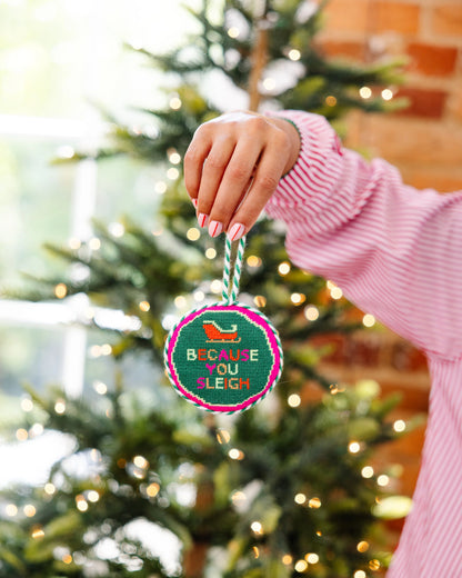 Hand holding a Christmas ornament with 'Because You Slept' text in front of a decorated tree.