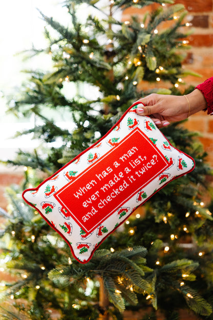 Hand holding a decorative pillow with text in front of a Christmas tree