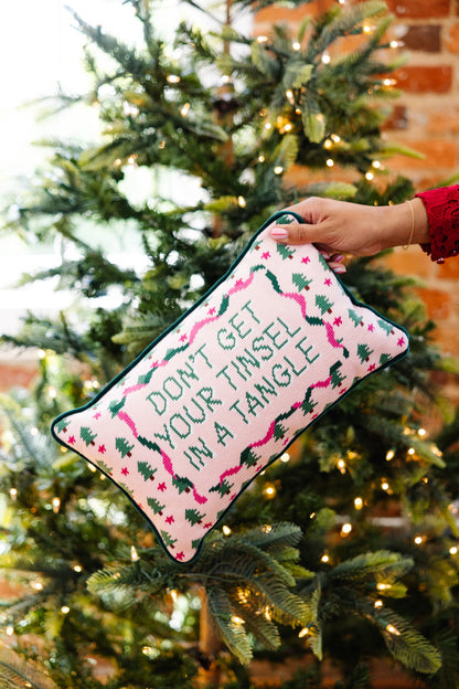 Decorative pillow with Christmas-themed text and patterns held in front of a decorated Christmas tree.