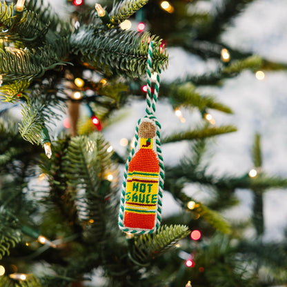 Decorative hot sauce bottle ornament on a Christmas tree with lights.
