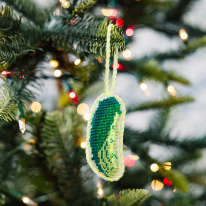 Decorative pickle ornament on a Christmas tree with blurred lights in the background