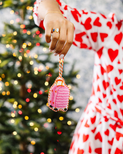 Person holding a pink gingerbread house ornament with a Christmas tree in the background