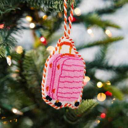 Pink suitcase ornament hanging on a Christmas tree with blurred lights in the background