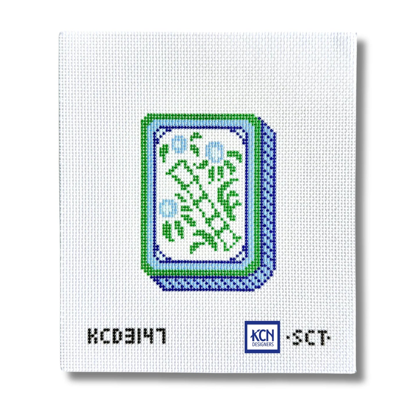 A square white needlepoint canvas featuring a pixelated green and blue card design in the center, with black alphanumeric text 'KCD3147' and a blue 'KCN Needle' logo at the bottom.