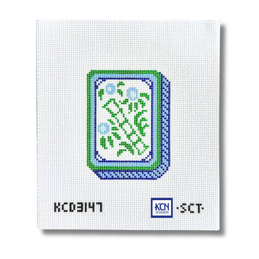 A square white needlepoint canvas featuring a pixelated green and blue card design in the center, with black alphanumeric text 'KCD3147' and a blue 'KCN Needle' logo at the bottom.