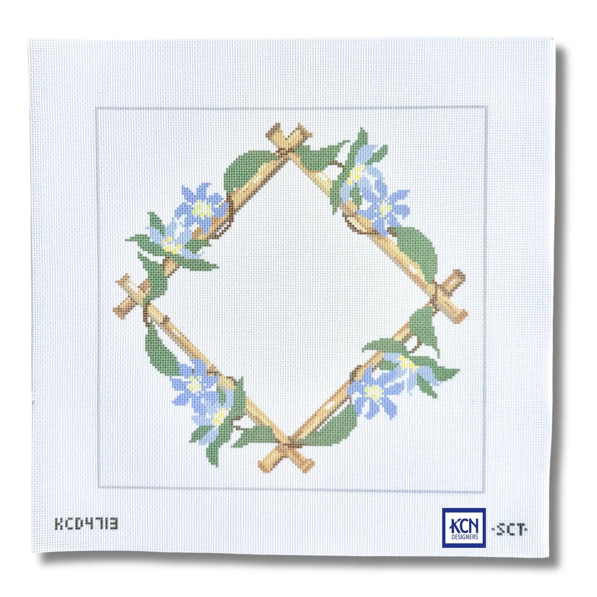 A needlepoint canvas featuring a diamond-shaped wreath design made of tan branches with green leaves and blue flowers, on a white canvas background with printed codes and a KCN logo.