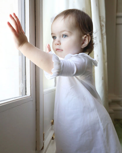 Child in a white dress standing by a window