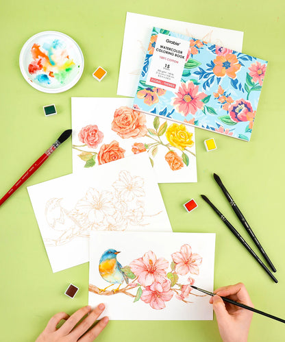 Art supplies including watercolor paper, brushes, and a colorful floral painting on a green surface.