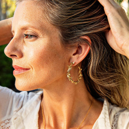 Woman wearing gold hoop earrings with a blurred natural background