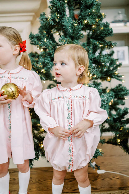 Two children in matching pink dresses standing in front of a decorated Christmas tree.