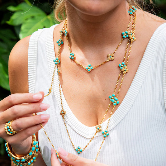 Woman wearing a gold and turquoise necklace with a white top outdoors