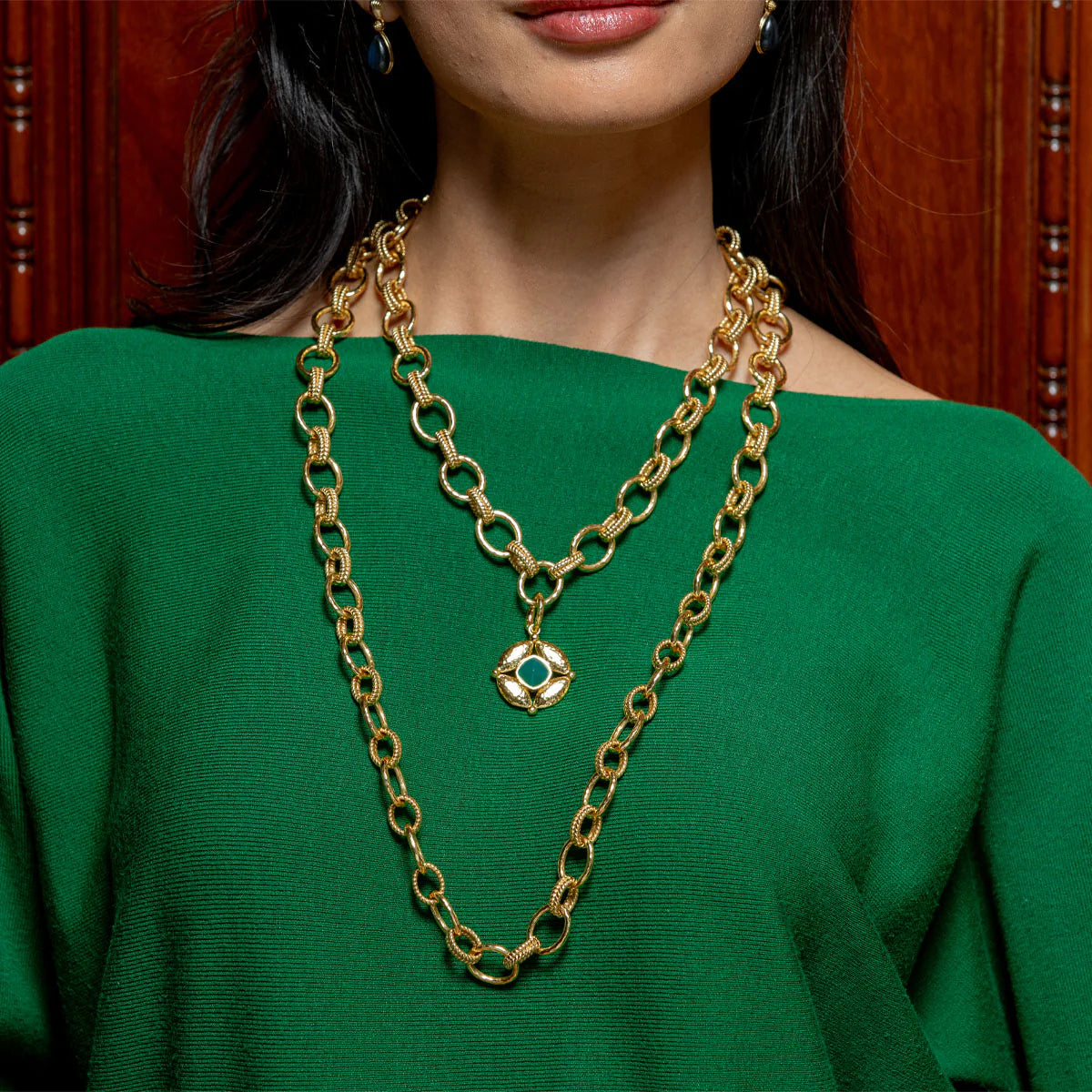 Gold chain necklace with a green gemstone pendant worn by a person in a green top.