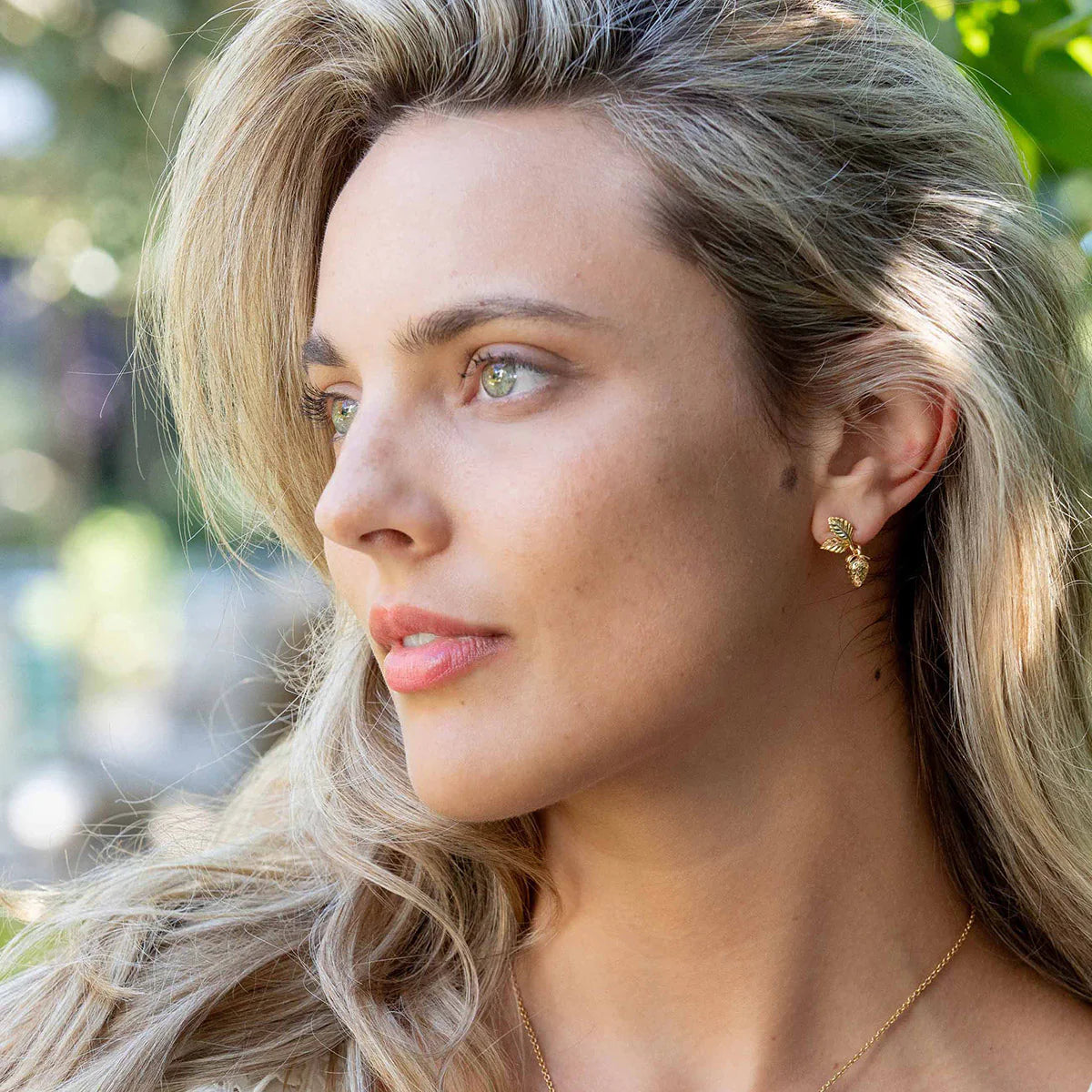 Woman with blonde hair wearing gold earrings and a necklace outdoors