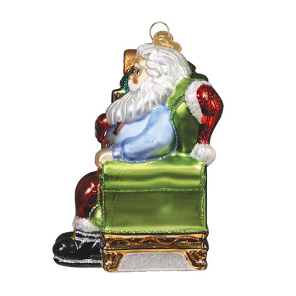 Glass ornament of Santa Claus sitting on a green chair with a white background