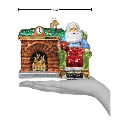 Glass ornament of Santa Claus by a fireplace with a clock, on a white background.