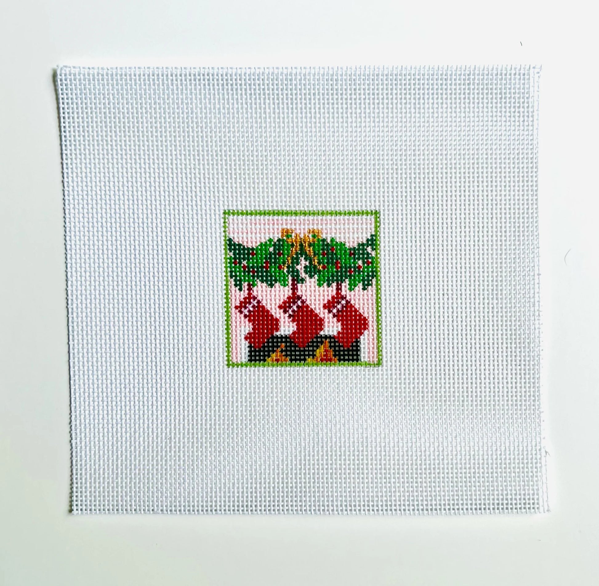 Cross-stitched design of stockings hanging by a fireplace on white fabric.