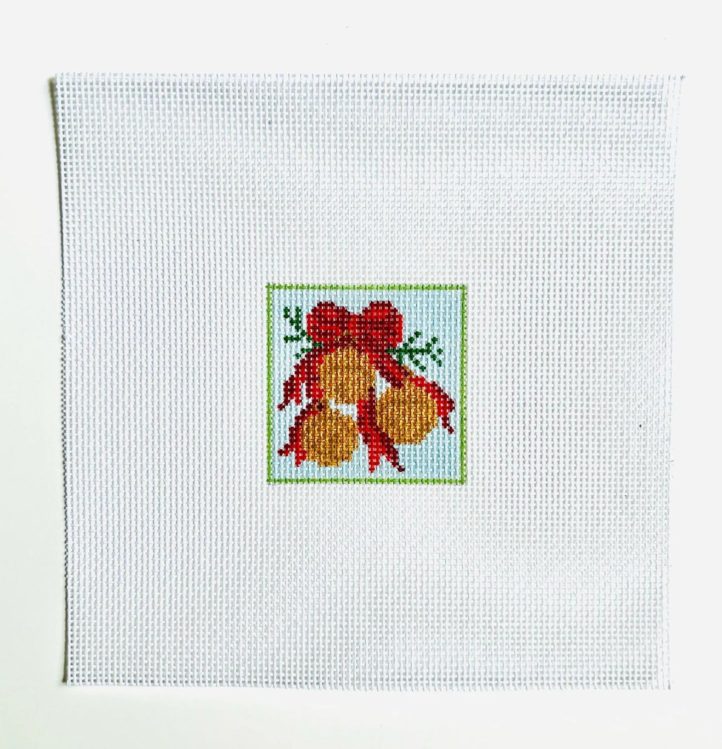 Cross-stitched design of a red bow with gold balls on white fabric