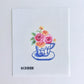 Cross-stitched design of a teacup with flowers on a white background