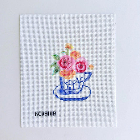 Cross-stitched design of a teacup with flowers on a white background