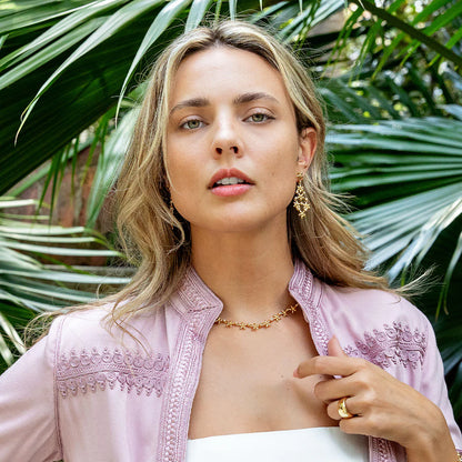 Woman wearing a pink embroidered top with a tropical background