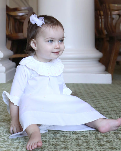 Young child in a white dress sitting on the floor with columns in the background