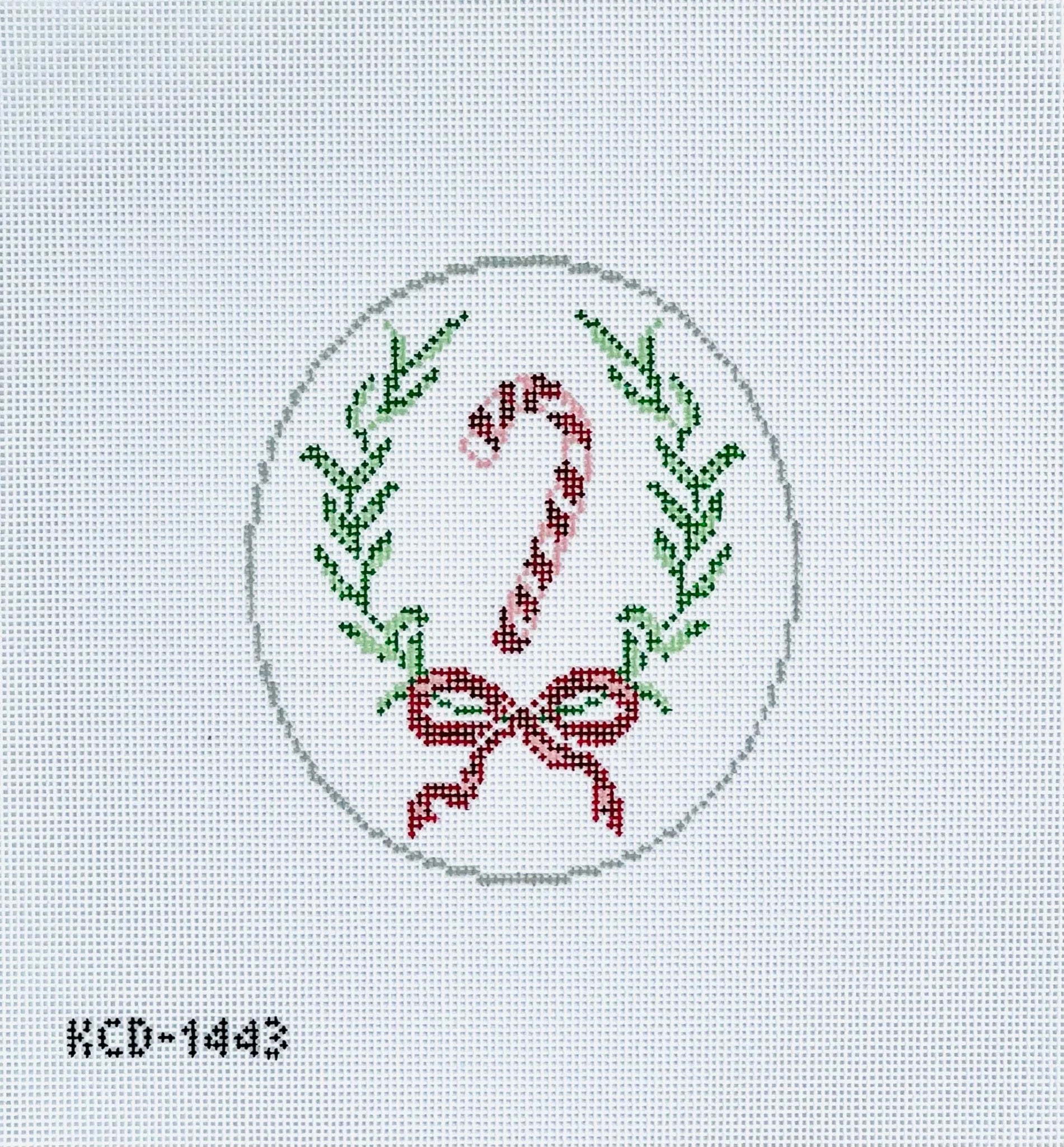 Cross-stitched design of a candy cane and bow with greenery on a light gray background.