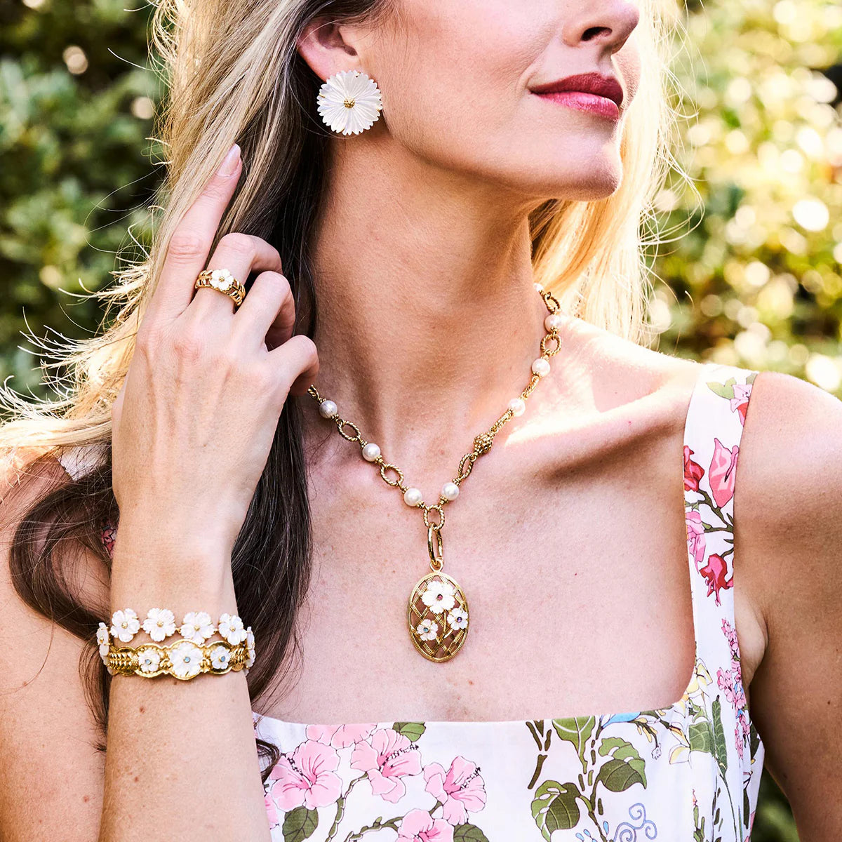 Woman wearing a gold necklace, earrings, and bracelet with a floral dress.