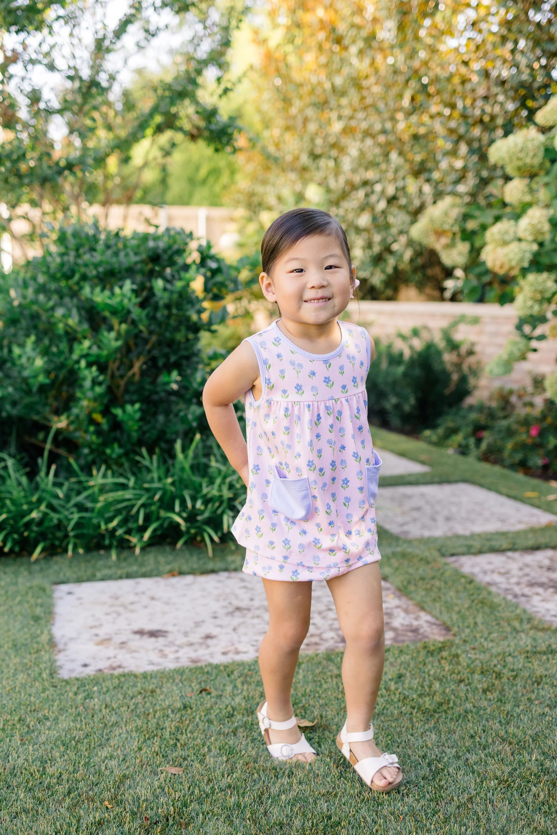 Young girl in a floral dress standing outdoors with greenery around