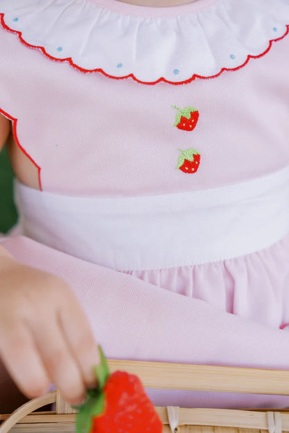 A pink baby bubble romper with white trim and strawberry appliques on the pockets and a ruffled collar.