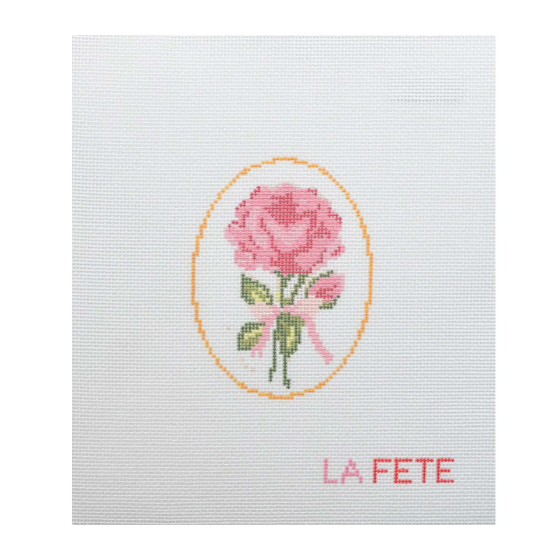 Cross-stitched design of a pink rose with a yellow border on white fabric, featuring the word 'LA FETE'.