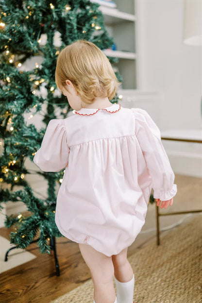 Child in a pink romper standing in front of a decorated Christmas tree.