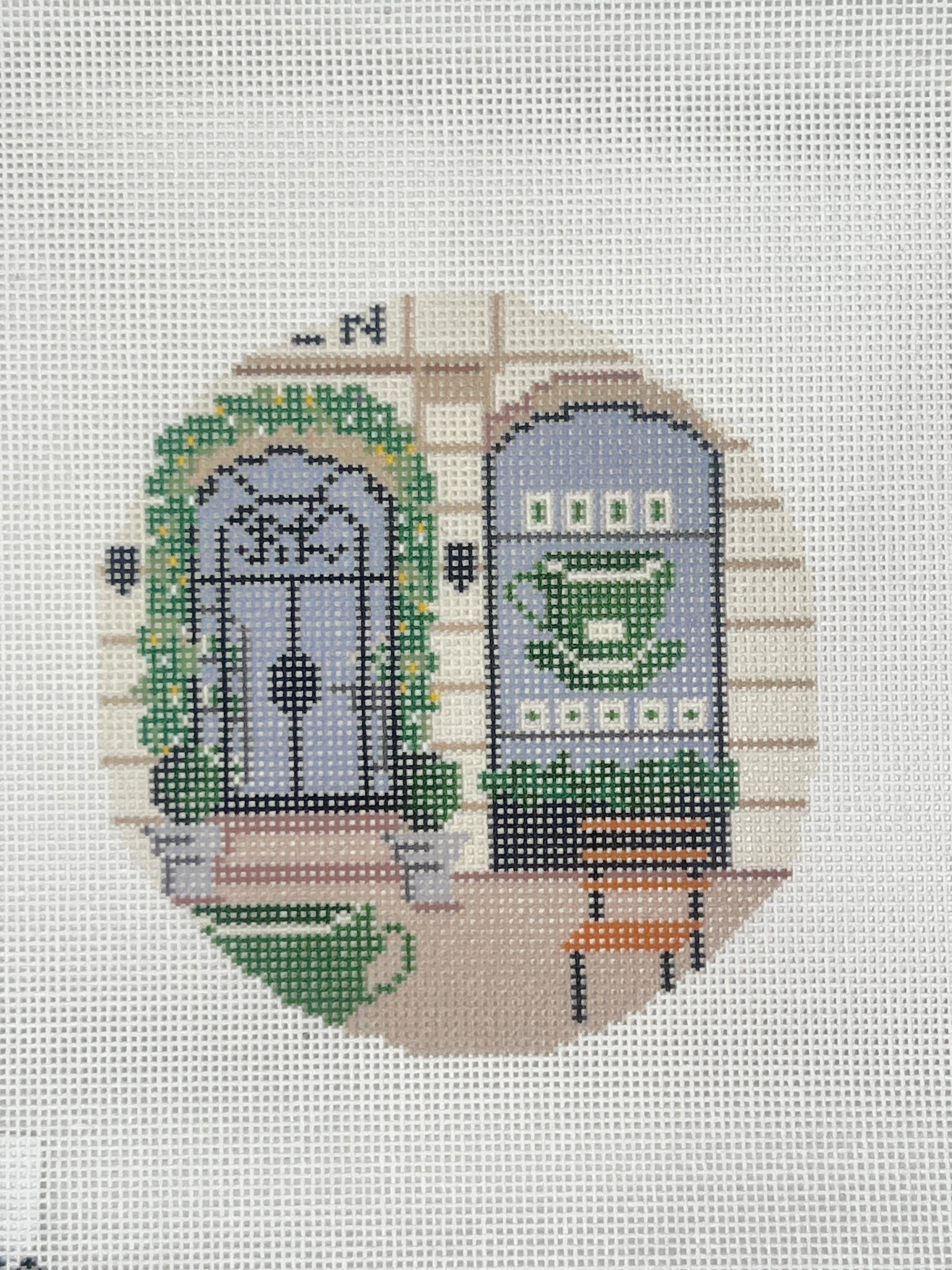 Cross-stitched design of a clog with a green pattern on a white fabric background