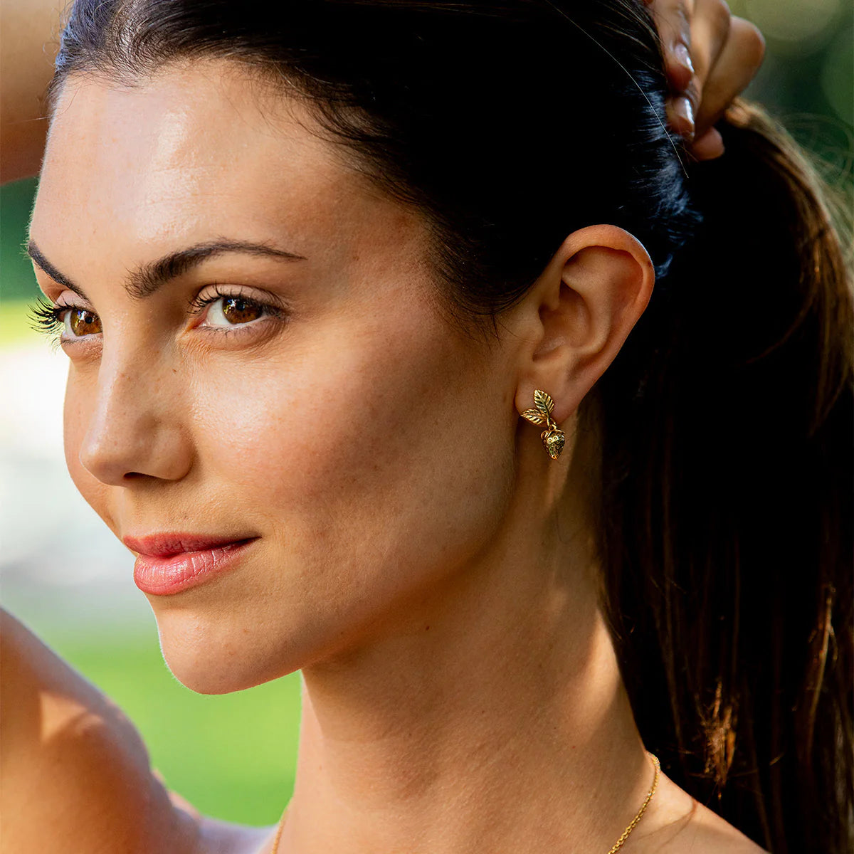 Close-up of a woman with a gold earring and necklace against a blurred green background