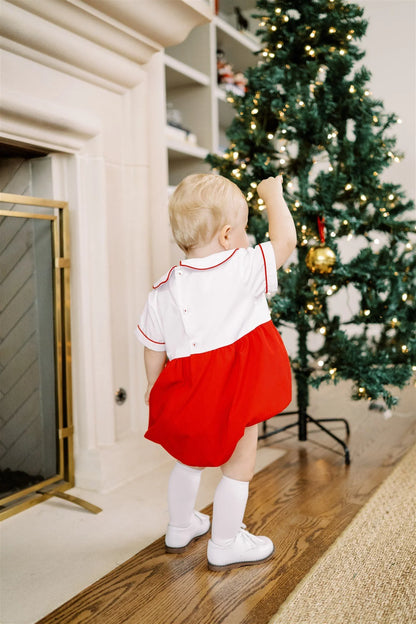 Child in a red and white outfit standing in front of a decorated Christmas tree.