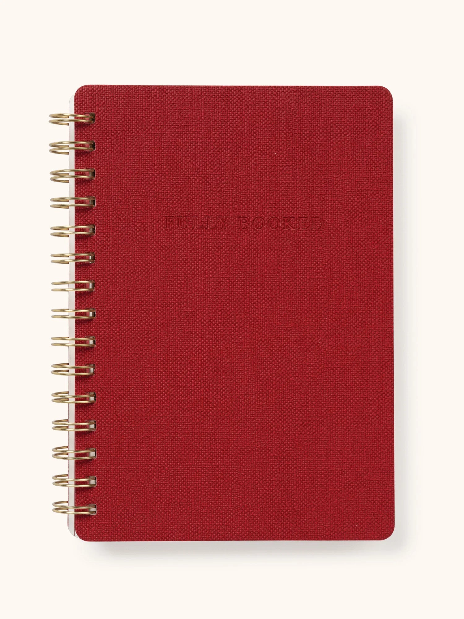 A red spiral-bound notebook with a textured cover and gold-toned wire binding, shown on a light cream background.