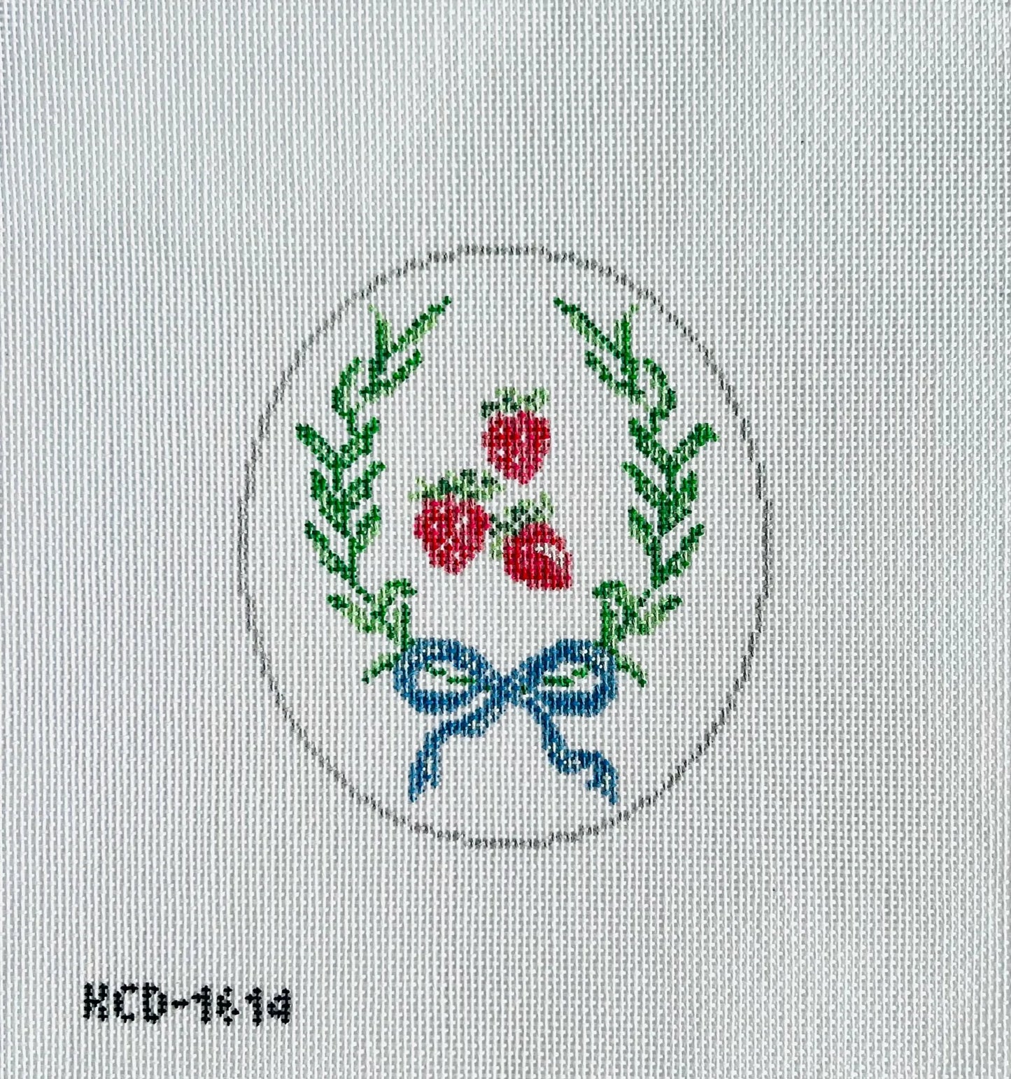 Embroidered design of a wreath with red berries and a blue bow on a white fabric background.