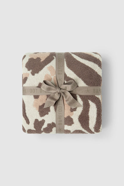 A folded plush throw blanket with a zebra-like animal print pattern in brown, beige, and cream, wrapped with a taupe ribbon that has the BARFOOT BAR brand name printed on it, set against a light gray background.