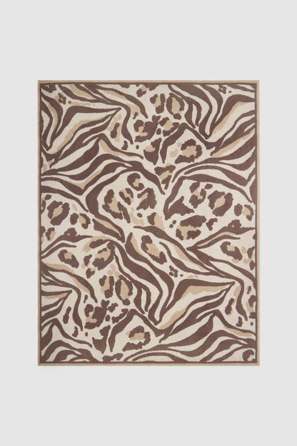 A rectangular area rug featuring an abstract zebra and leopard print pattern in shades of brown, beige, and cream, shown flat against a light gray background.