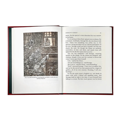 An open book with a dark red cloth-bound cover, showing printed text and a black-and-white illustration on the left page, photographed against a plain white background.