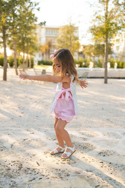 Young girl in a pink outfit standing on sand with trees and buildings in the background