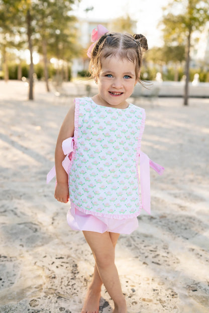 Young girl in a patterned dress standing outdoors with trees in the background.