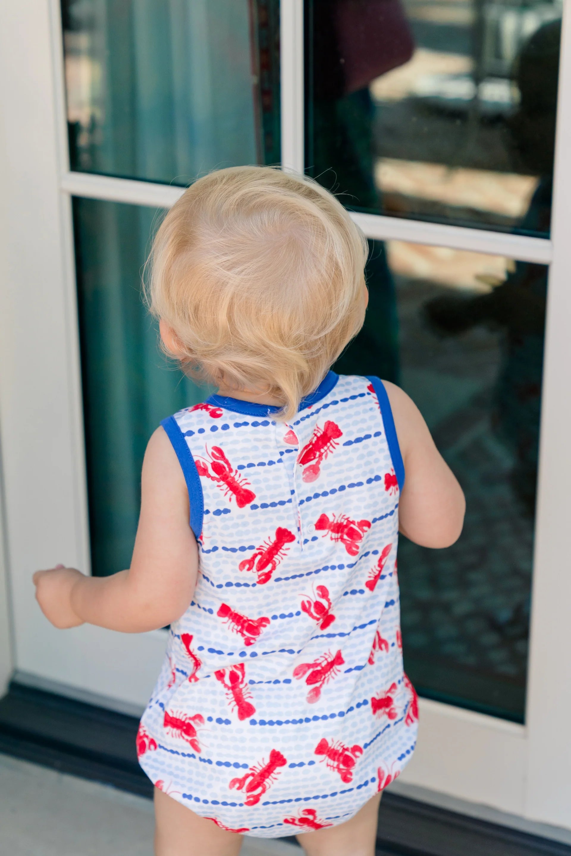 Child wearing a sleeveless shirt with red lobster print standing in front of a glass door.