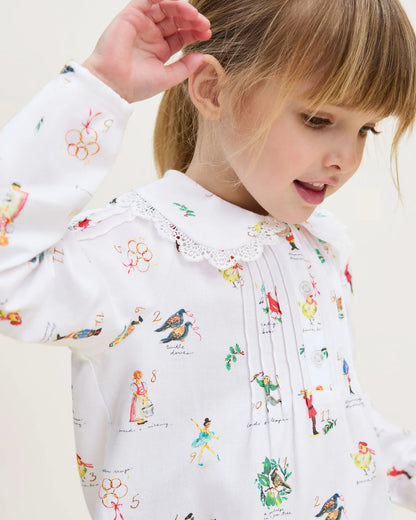Child wearing a white blouse with colorful printed designs on a light background
