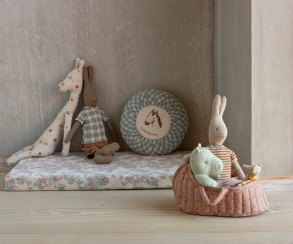 Children's toys including a giraffe, rabbit, and other plush items on a floral mattress against a neutral wall.