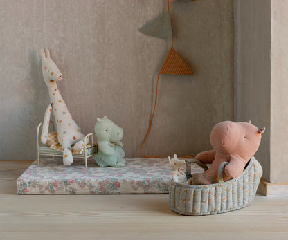 Children's room with stuffed animals on a floral bedspread and wall decorations.